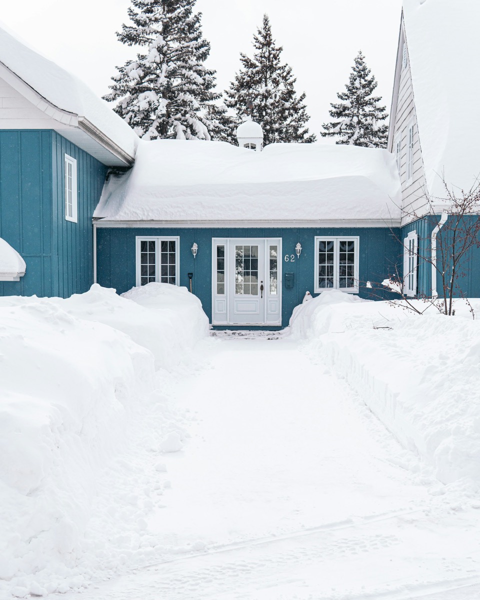 Maison de bois bleue derrière un banc de neige